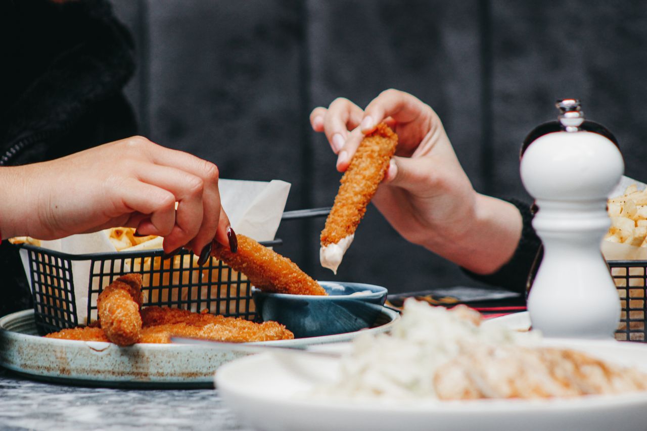 Enjoying crispy chicken fingers with dip during a shared meal at a cozy restaurant.