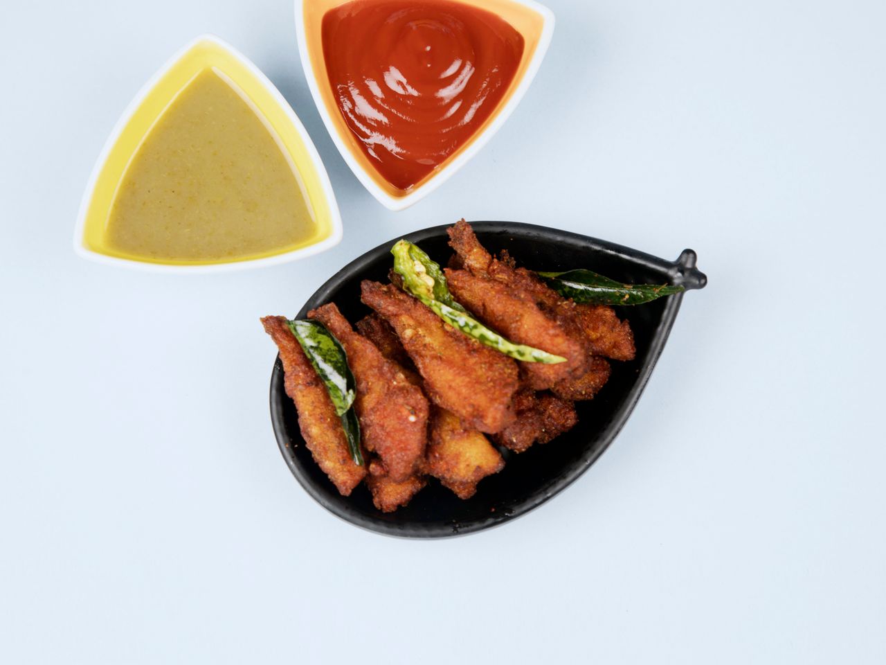 Delicious crispy chicken wings served with spicy ketchup and mustard sauce on a light blue background.